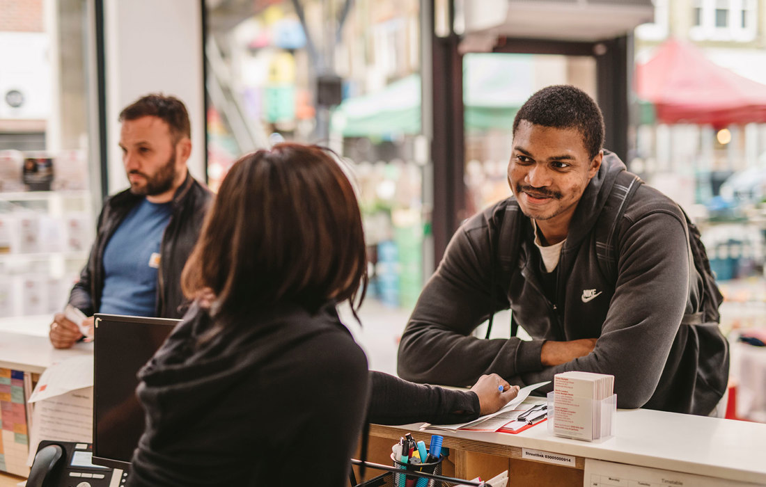 A man stands at a desk talking to a receptionist at Crisis Skylight centre.