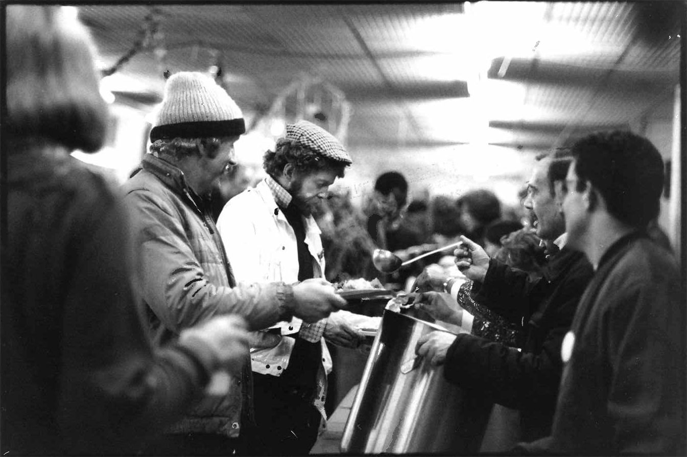 A black and white archival photograph of guests queuing for food at an early Crisis at Christmas. 