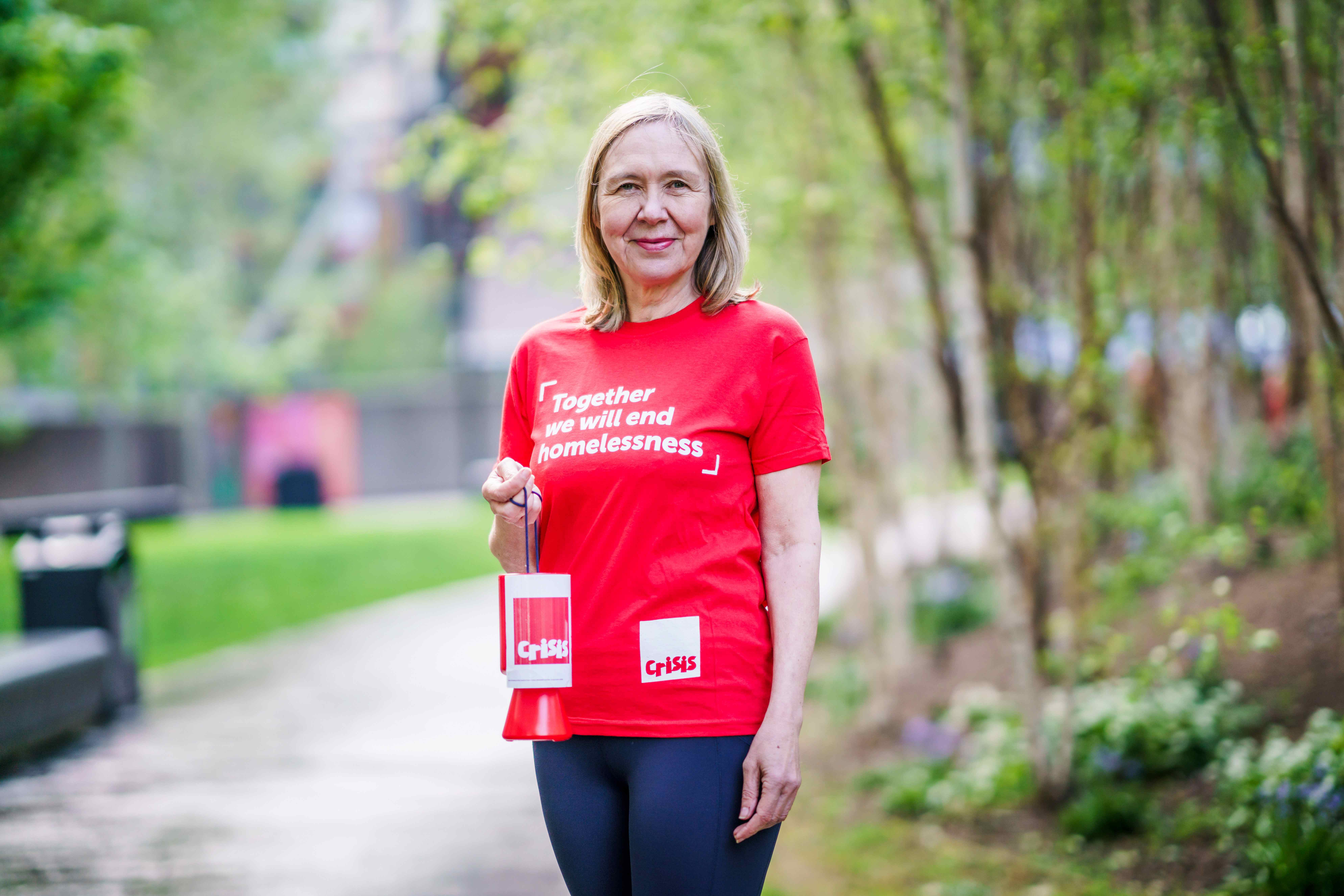 A woman wearing a Crisis branded top holding a collection bucket