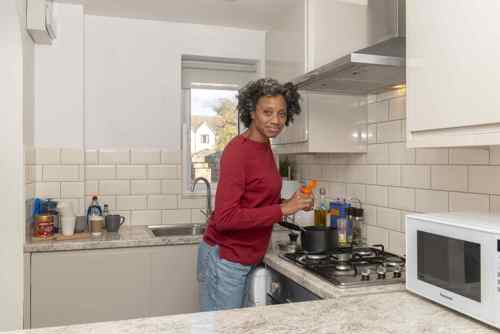 Middle aged black woman with natural hair stands in clean and tidy kitchen holding spices while cooking a meal