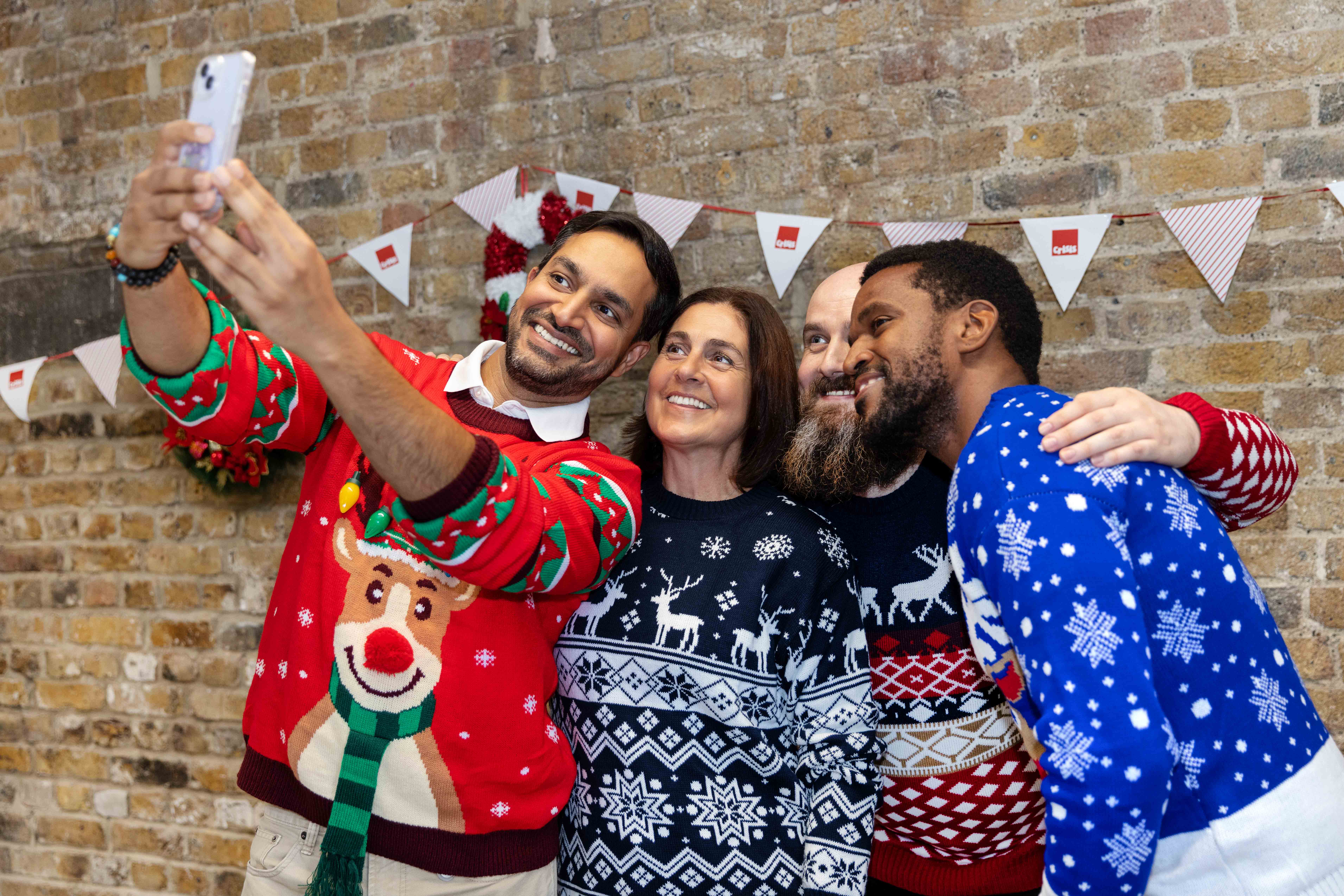 Four people in Christmas jumpers smiling and taking a selfie.