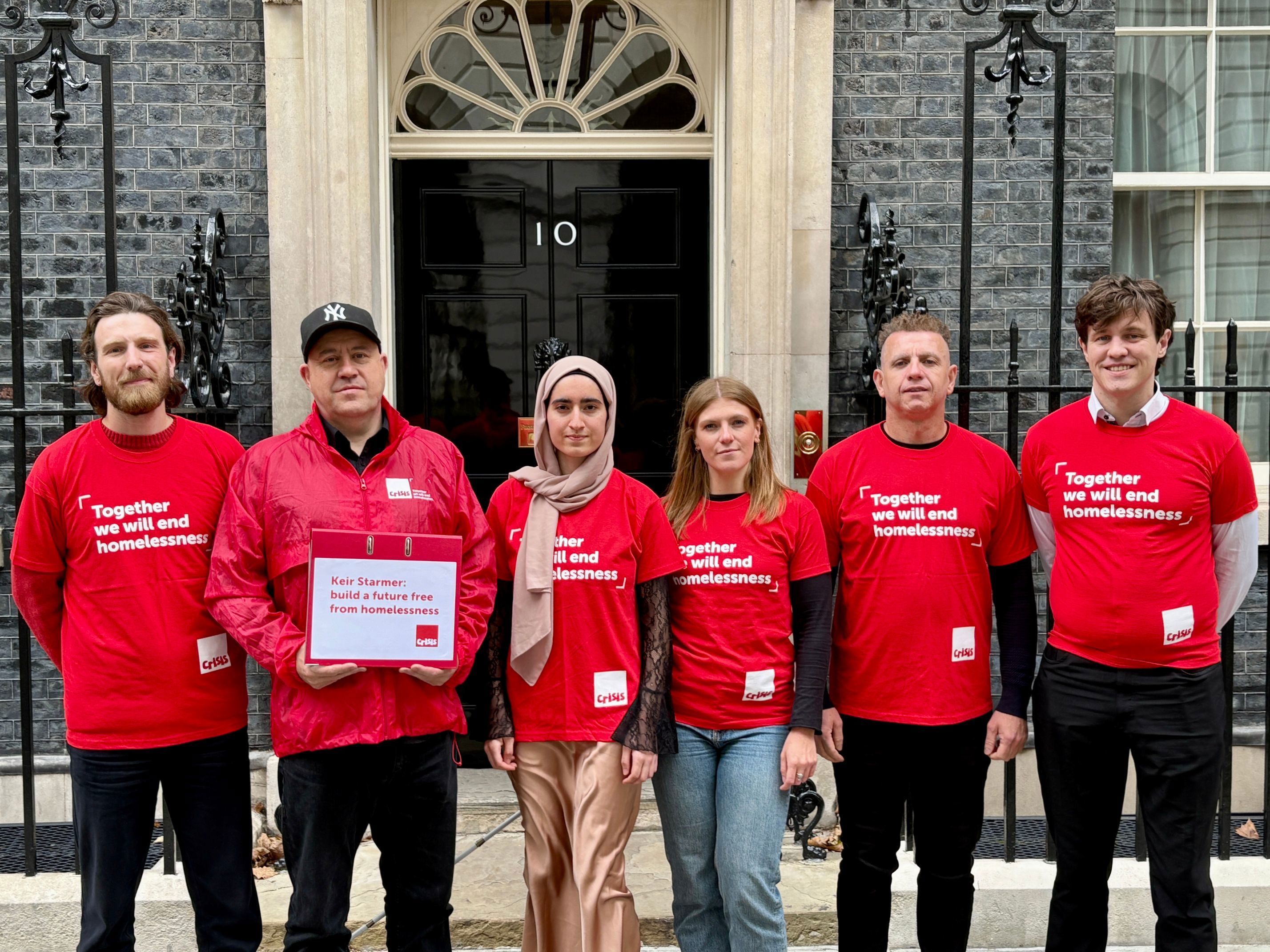 Six people wearing red Crisis t-shirts stand outside the black door of Number 10 Downing Street.