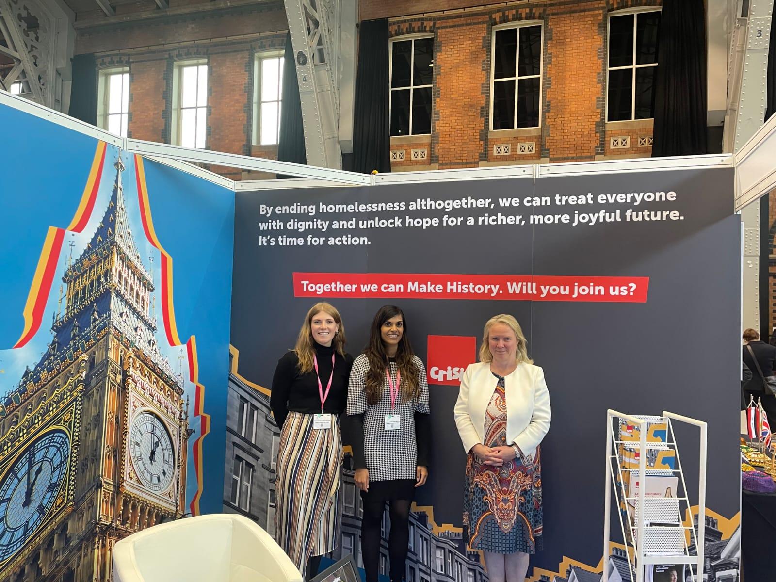 Two Crisis staff and the minister for homlessness, Felicity Buchan, standing in front of the Crisis stand at the Conservative Party Conference.