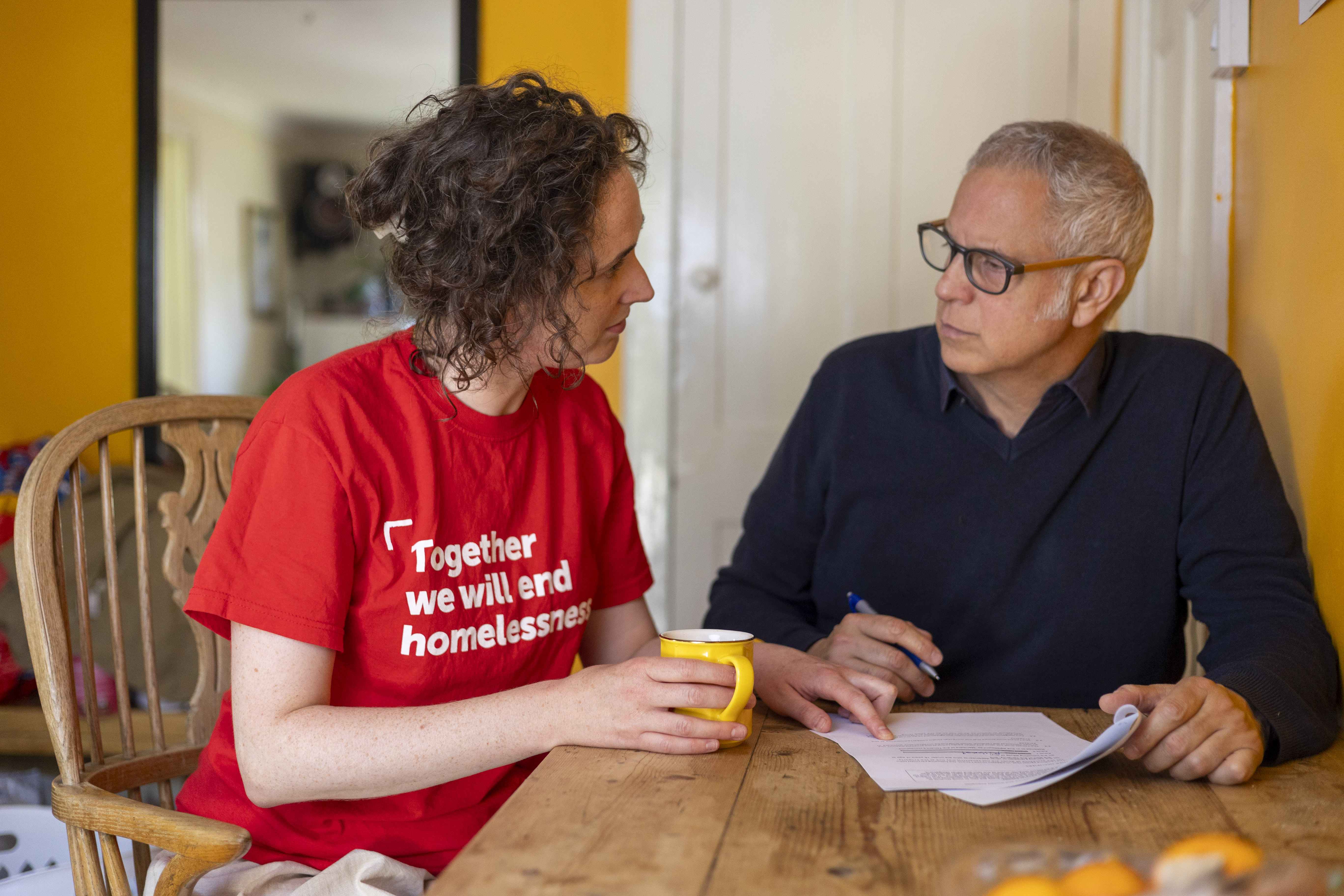 Massimo and a Crisis staff member are sat at a dining room table together. They are filling in a form while drinking tea. 