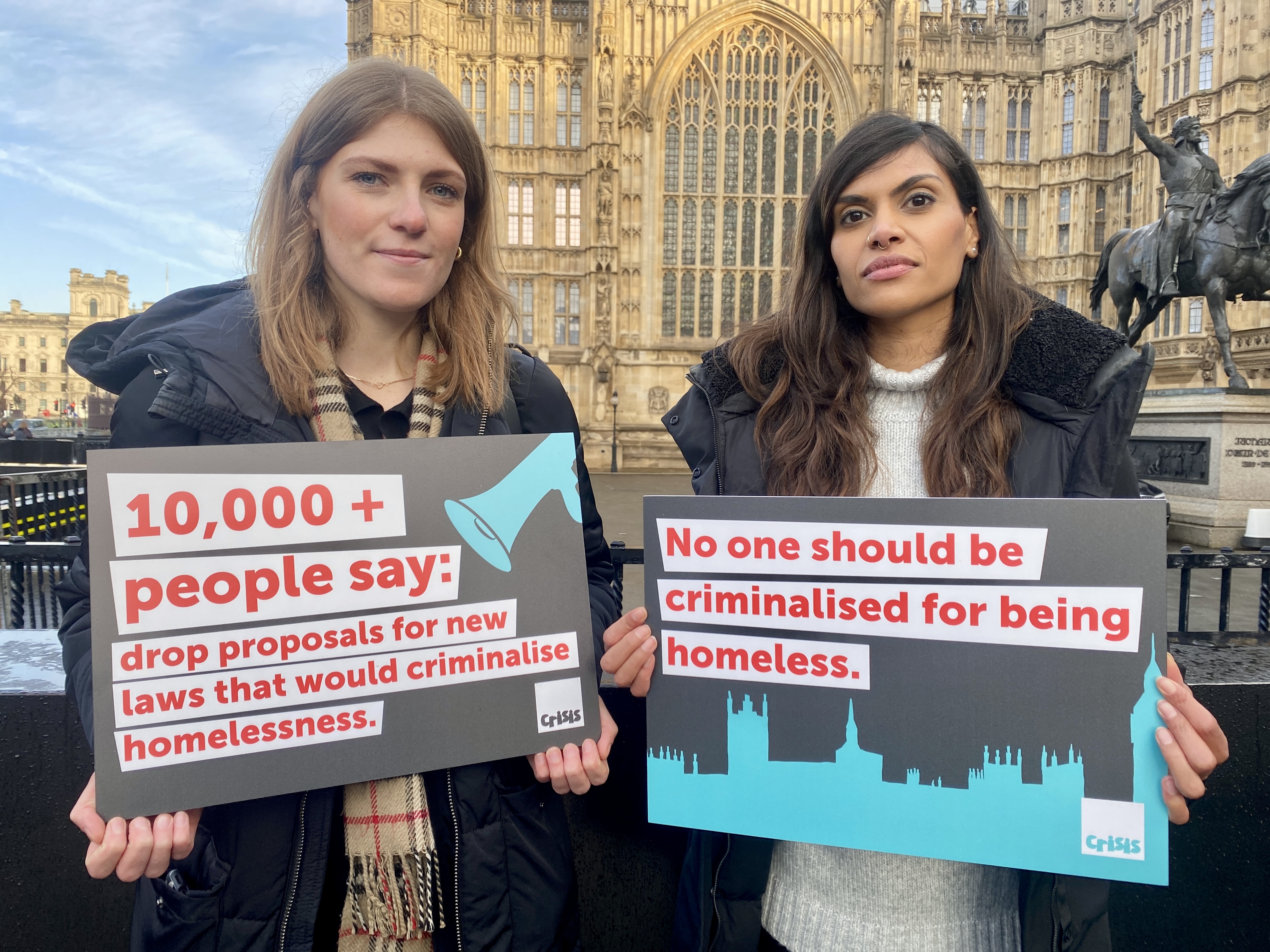 Two women standing in front of the Houses of Parliament holding campaign boards that say: no one shoukd be criminalised for being homeless.