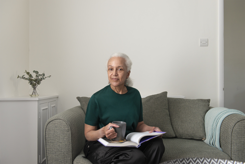 Yasmin reading on her sofa, she has grey hair and is drinking a cofee