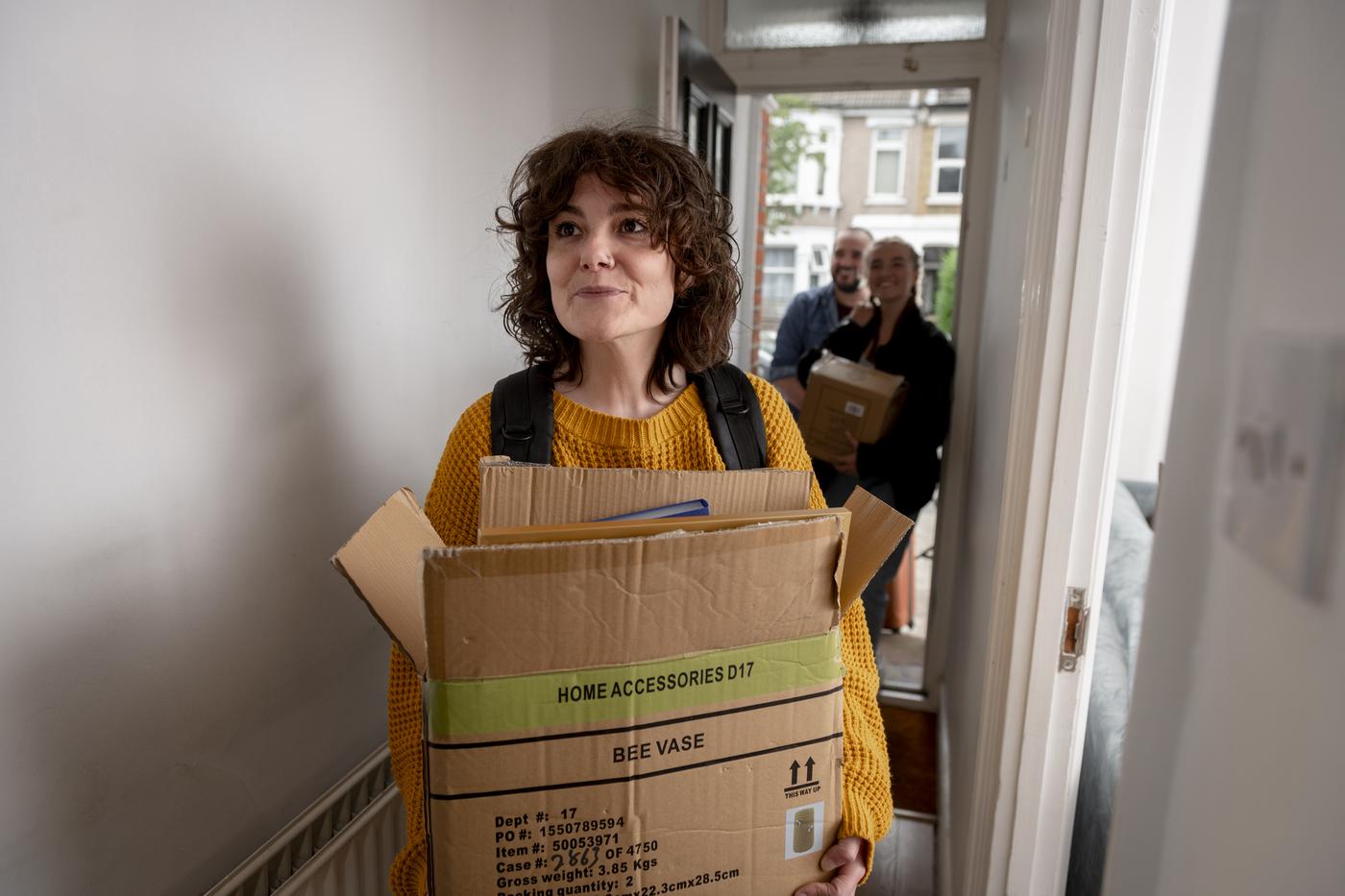 A woman standing in the hallway of a house holding a cardboard box